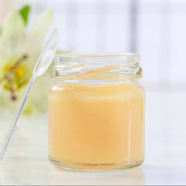 Glass jar with a yellowish substance and a spoon on a white background