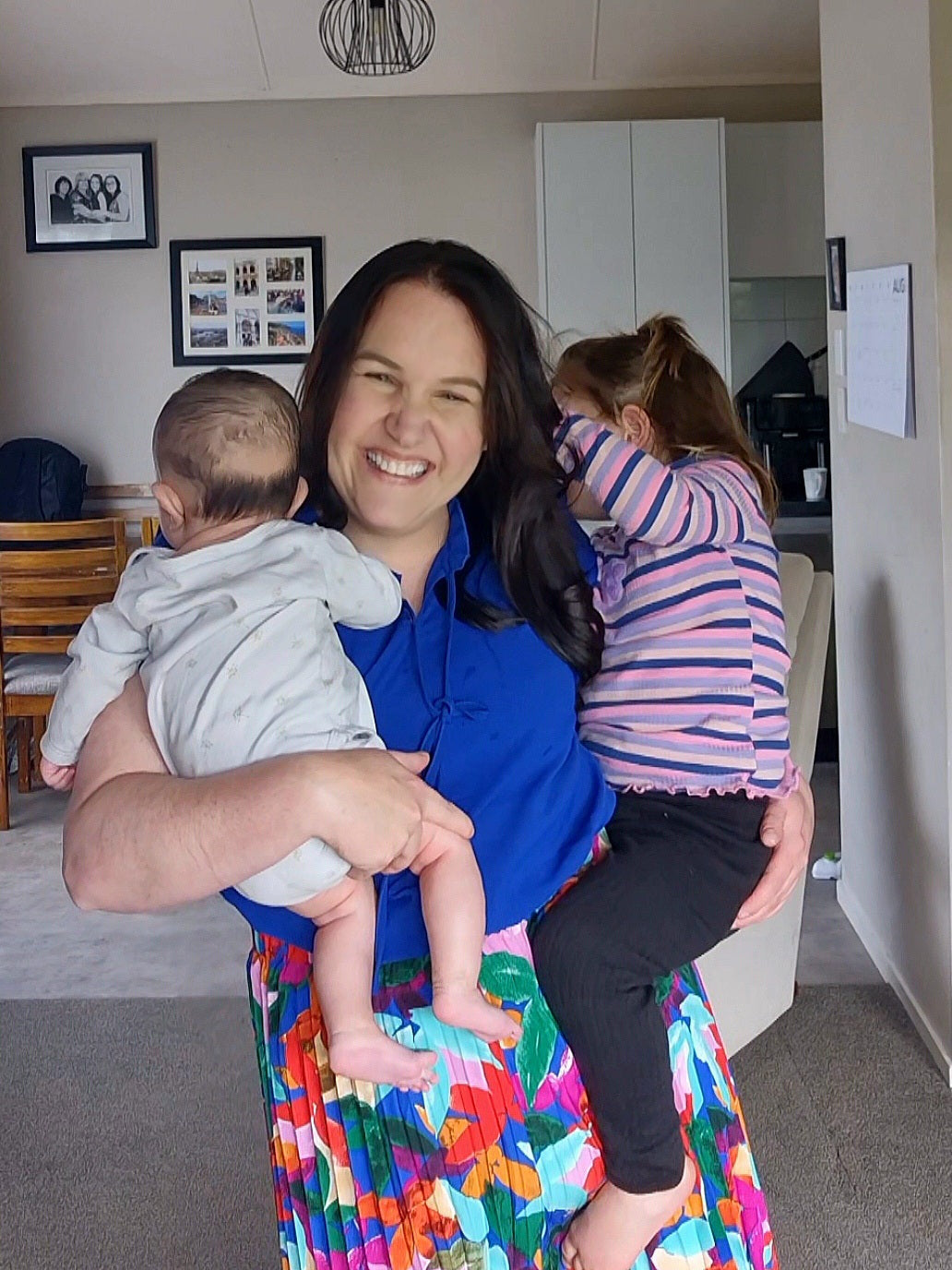 Woman holding a baby and standing next to a child in a colorful room.
