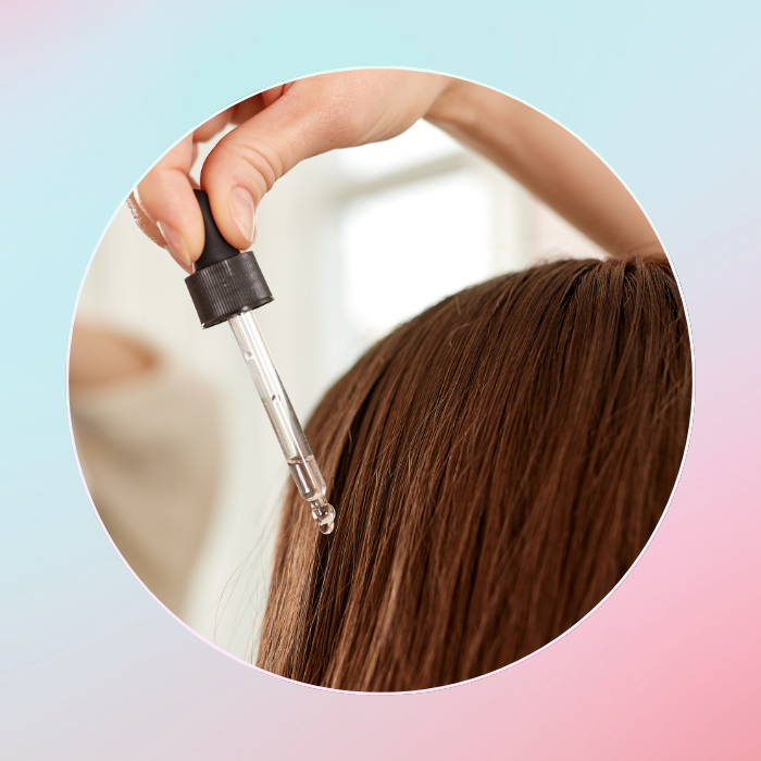 Hand using a dropper to apply a liquid to hair on a gradient background