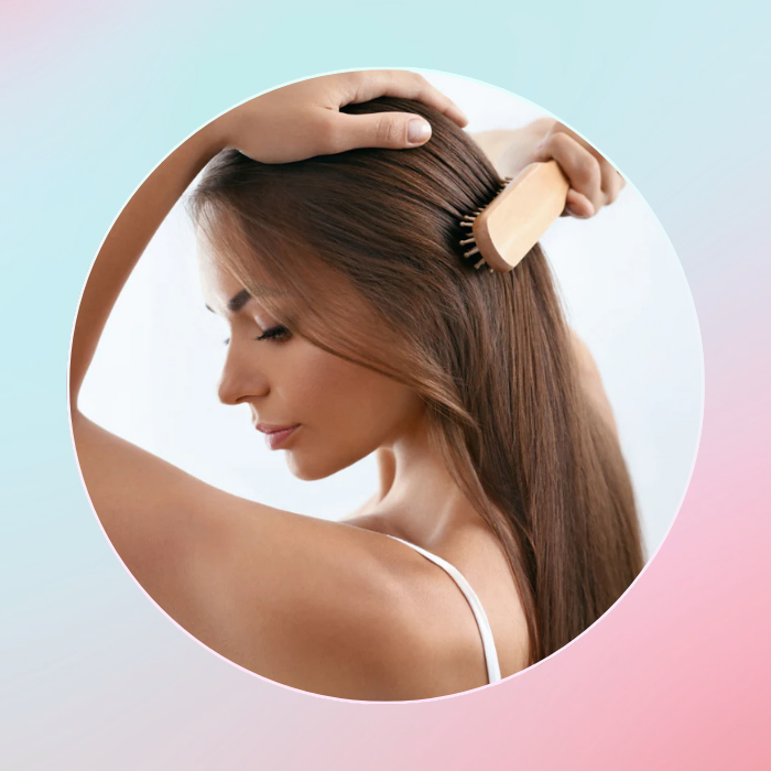 Woman brushing her hair with a wooden brush against a gradient background