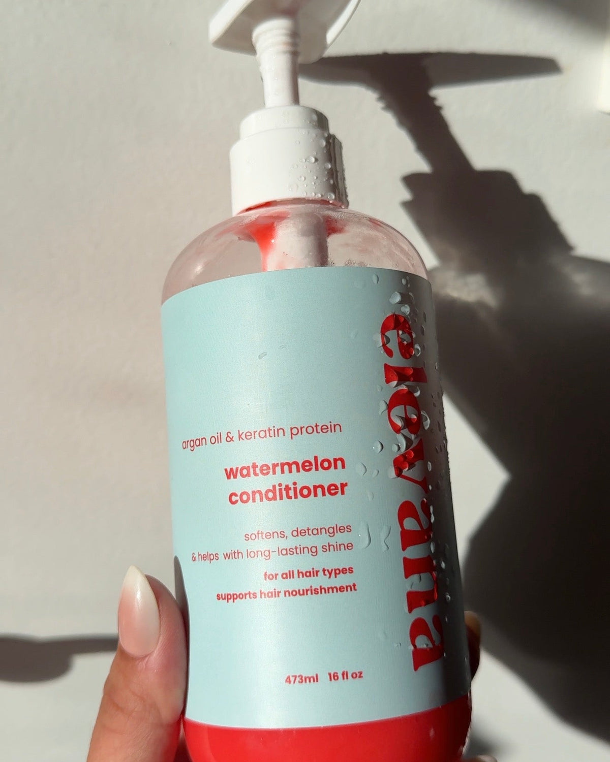 Hand holding a bottle of watermelon conditioner with visible text on a white background.