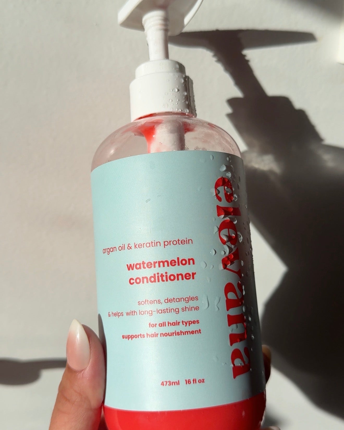 Hand holding a bottle of watermelon conditioner with visible text on a white background.