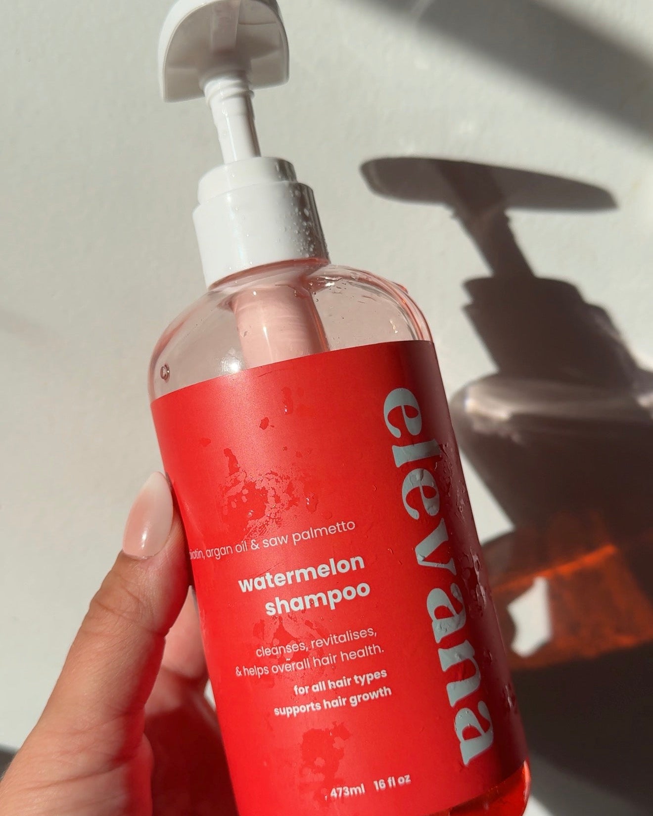 Hand holding a bottle of Elevate shampoo with a blurred background