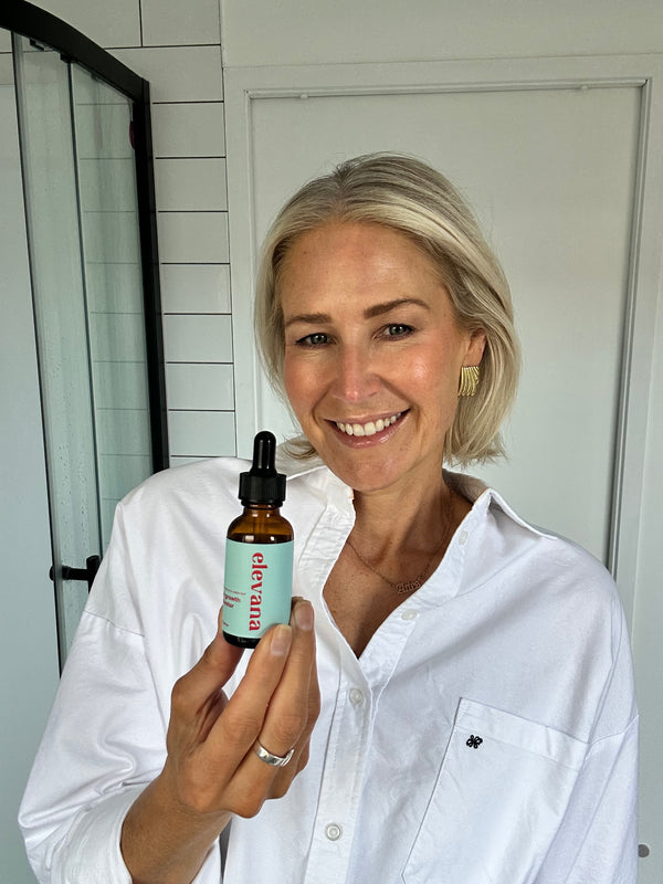 Person holding a bottle labeled 'elevana' in a bathroom setting