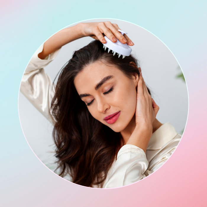 Woman using a scalp massager with a pastel gradient background