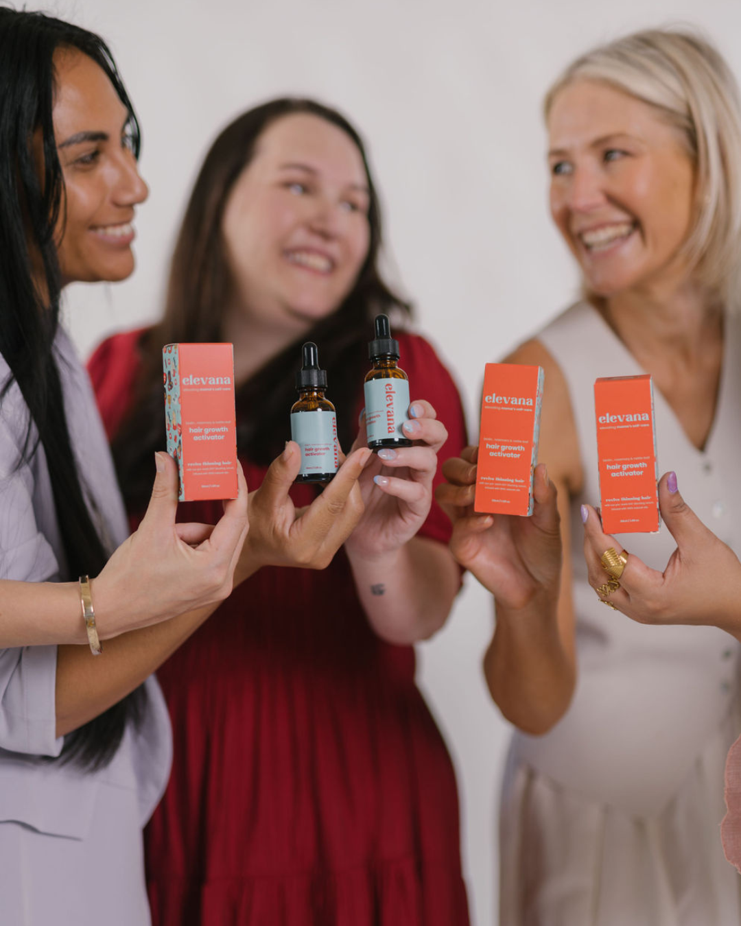 Three women holding hair care products with a plain background
