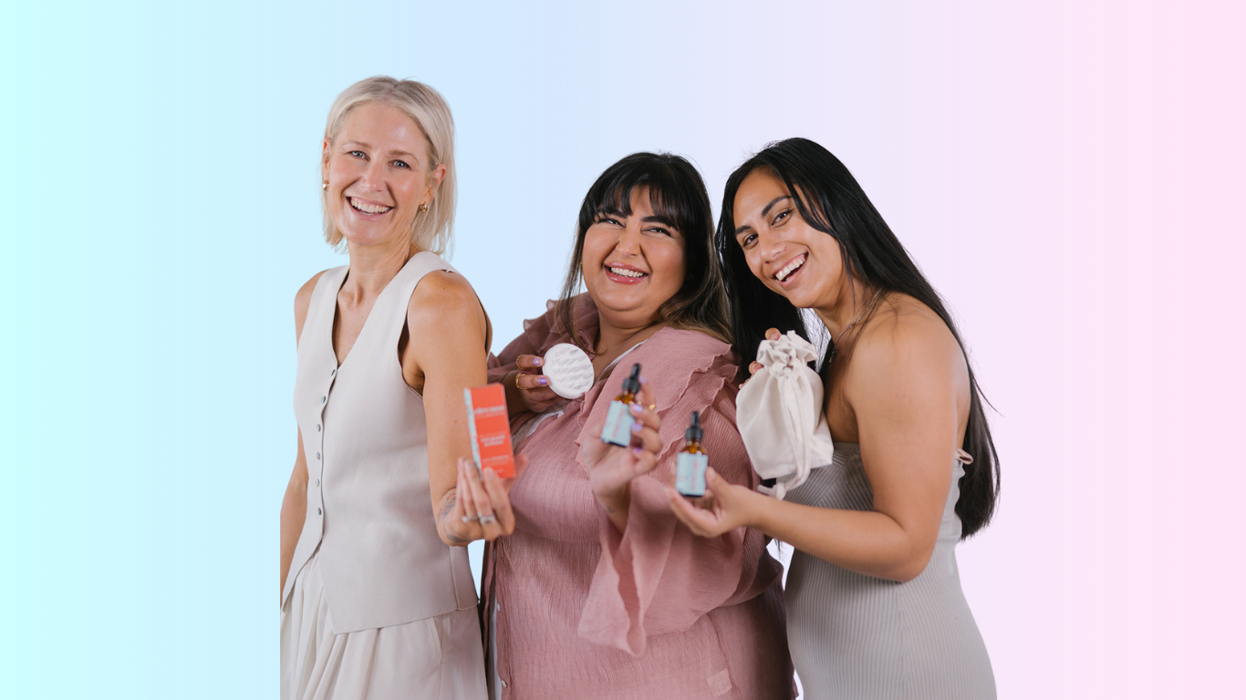 Three women holding hair care products against a gradient background