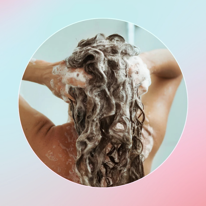 Person washing hair with shampoo against a gradient background